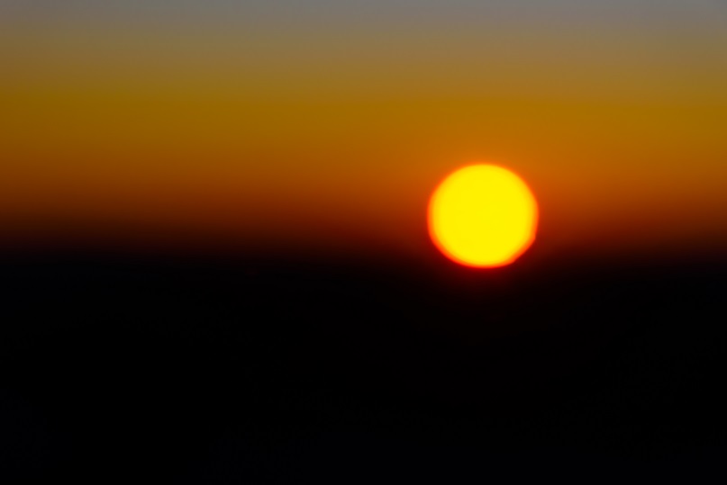Sunrise in Australia; a dramatic contrast of red and black behind the gold disc of the sun; the image is reminiscent of the iconic Australian Aboriginal flag